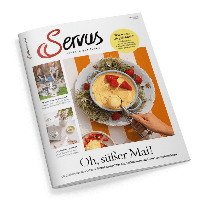 Cover des Servus Magazins, Mai 2025, mit einer Schale gelbem Eis und frischen Erdbeeren auf einem orange-weiß gestreiften Hintergrund. Eine Hand schöpft Eis. Titel: Oh, süßer Mai!