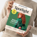 Schräg gehaltenes englischsprachiges Magazin „Spotlight“ in den Händen einer weiblichen Person mit beigem Strickpullover. Das Cover zeigt eine rothaarige Person im grünen Oberteil und trägt die Texte „ENGLISCH“, „ZEITSPRACHEN“, „Das Magazin zur englischsprachigen Welt“, „English Decoded – Understanding what we say – and what we really mean“ sowie „The Big Report: Canada a better USA?“, „Sri Lanka“, „The Blues“ und „Milk-Float Memories“.