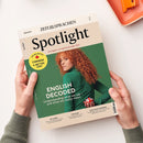 Englischsprachiges Magazin „Spotlight“ von ZEIT SPRACHEN, schräg von oben auf weißer Fläche und von zwei Händen gehalten. Das grüne Cover zeigt eine rothaarige weibliche Person mit Union-Jack-Ball sowie die Texte „ENGLISH DECODED“, „Understanding what we say – and what we really mean“, „THE BIG REPORT CANADA A BETTER USA?“, „SRI LANKA“, „THE BLUES“ und „MILK-FLOAT MEMORIES“; oben rechts liegt ein orangefarbenes Notizbuch.